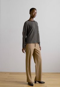 Black and white striped sweater with a v-neck, paired with light brown wide-leg trousers and pointed black heels against a neutral background.