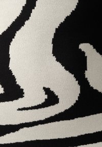 Schwarz-weiß gestrickter Stoff mit einem wellenförmigen abstrakten Design, das kontrastierende Formen und Texturen aufweist und ein auffälliges visuelles Muster erzeugt.