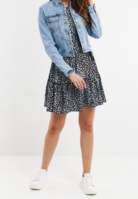 Chaqueta de mezclilla sobre un vestido negro con flores y volantes; zapatillas blancas; el patrón floral presenta colores pastel sobre un fondo oscuro.