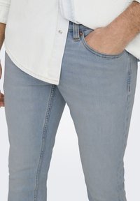 Jeans de mezclilla azul claro con un ajuste slim, que presentan una textura suave, costuras en contraste y un bolsillo en la cadera.
