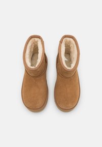 Bottines en daim tan avec une doublure en fausse fourrure crème douce et un bout arrondi. Présente un design simple et des accents cousus au niveau du col.