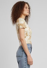 Kuttet t-skjorte med kort erme i beigemønstret kamuflasje; myk bomullsblanding med en tettsittende design; stylet med høyhårede lyseblå jeans.