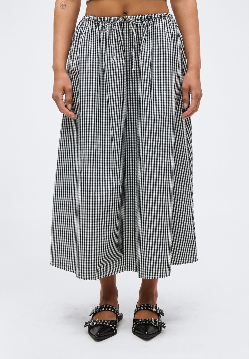 Μίντι ασπρόμαυρη φούστα γκίνχαμ με δέσιμο στη μέση, φορεμένη με μαύρα μυτερά παπούτσια με τρουκς, εμφανίζεται από τη μέση έως τα πόδια.