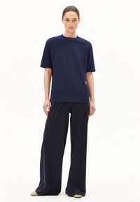 Donkerblauwe, korte mouwen t-shirt gecombineerd met brede donkerblauwe broek, beide in zachte stof. Opvallende details zijn de simpele lijnen en de relaxte pasvorm.