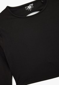 Zwart cropped top van glad, rekbaar materiaal met een ronde halslijn en lange mouwen, met een label waarop maat 'S' en de merknaam staat.