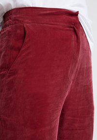 Pantalons en velours bordeaux avec une taille élastique et des poches latérales, offrant une texture douce et une finition lisse.