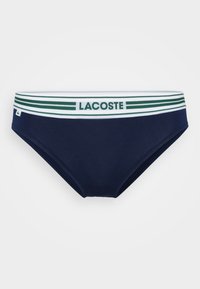 Tamsiai mėlynos spalvos maudymosi kelnaitės su balta ir žalia juostele, elastine juosta, ant kurios yra "LACOSTE" logotipas. Lygi tekstūra ir prigludęs dizainas.