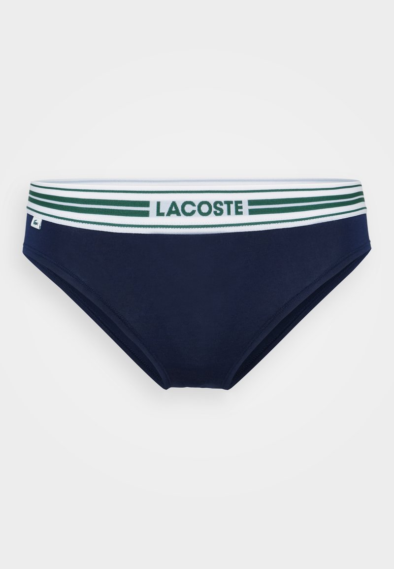Slip da bagno blu navy con un elastico in vita a strisce bianche e verdi, caratterizzato dal logo "LACOSTE". Texture liscia e design aderente.