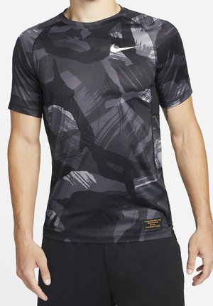Homme portant un t-shirt de sport Nike à manches courtes avec un motif abstrait noir et gris et un short noir, debout les bras détendus.