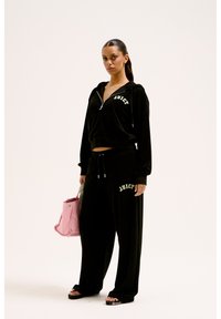 Completo in velour nero composto da felpa con zip e lettering "JUICY", pantaloni a gamba larga con logo abbinato, completato da una borsa rosa.