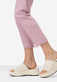 Sandali platform beige con cinturini larghi, indossati con pantaloni rosa chiaro a 3/4 con orli sfrangiati e una texture liscia.