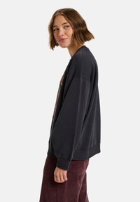 Zwarte oversized sweatshirt met een ronde hals, verlaagde schouders en een kleurrijk bloementekening op de voorkant; gecombineerd met corduroy broek.