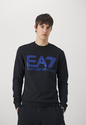 Felpa nera realizzata in un tessuto morbido, caratterizzata dai loghi blu EA7 ed Emporio Armani in una tipografia audace e moderna. Maniche lunghe con polsini a costine.