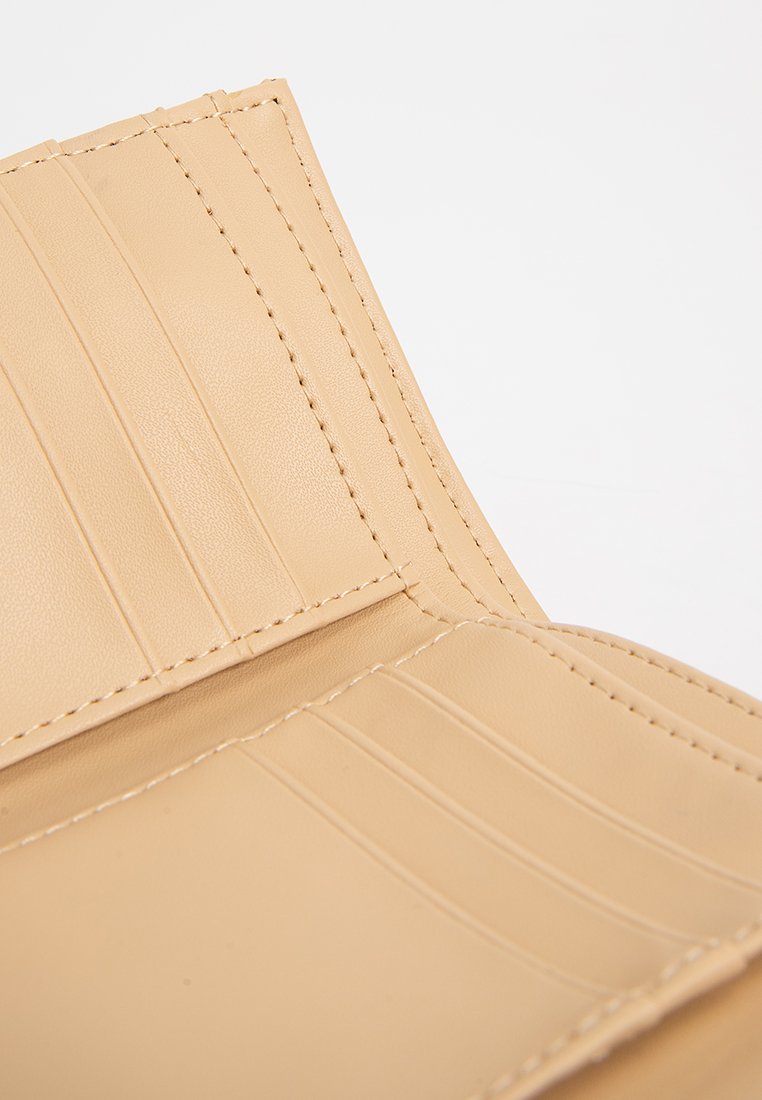 Beżowe skórzane wnętrze portfela z wieloma kieszonkami na karty, gładka tekstura i staranne przeszycia wzdłuż krawędzi.