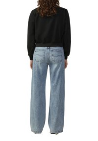 Zwarte cropped jas met geribbelde zoom, gecombineerd met loszittende, lichtblauwe denim jeans met twee achterzakken en een vervaagde textuur.