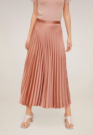 Jupe midi plissée en satin rose doux, dotée d'une large taille. Associée à des sandales à talons blocs blanches.