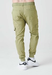 Pantalones cargo verde oliva con puños elásticos en los tobillos, dos bolsillos laterales y dos bolsillos traseros, combinados con zapatillas Nike blancas.