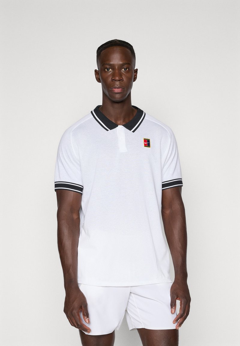 Camisa polo blanca con cuello negro y rayas en las mangas. Presenta un tejido texturizado y un pequeño logo colorido en el lado izquierdo del pecho.