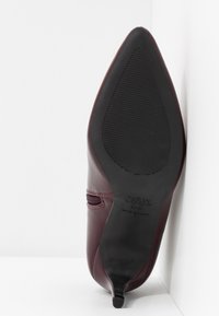 Chaussure en cuir bordeaux à bout pointu avec une semelle en caoutchouc noir portant la mention "NEW LOOK 41/37 Made in China" sur la semelle.