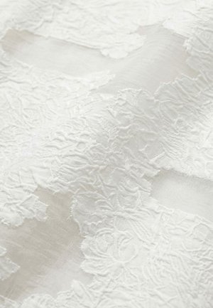 Weißer Stoff mit filigraner floraler Spitzenstickerei, die über durchsichtigem Material liegt und Textur sowie zarte Muster zeigt.