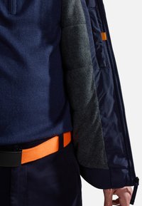 Blå jacka med grå fleeceärmar, prydd med orange bälte och detaljer. Slät yttertyg, strukturerad väv för värme och komfort.