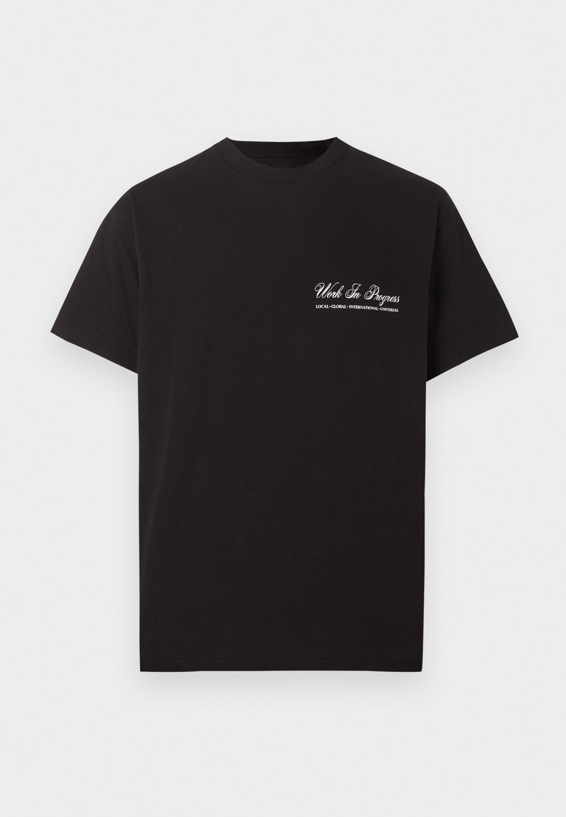 T-shirt nera a maniche corte con collo a girocollo, con testo bianco "Work In Progress" e testo più piccolo sotto, posizionato sul lato sinistro del petto.
