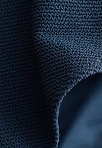 Tela azul oscuro con un patrón de punto texturizado y ondulado, doblada sobre una tela lisa y sólida azul oscuro debajo.