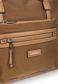 Sac en tissu marron à la surface texturée, doté d'une poche zippée à l'avant, d'accents en cuir beige et d'une fermeture éclair en métal avec un tirant.