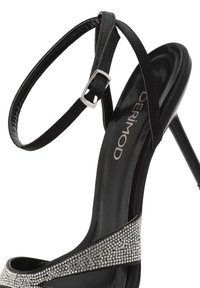 Sandalo nero con tacco alto dalla superficie brillante, dotato di una fibbia scintillante, cinturino alla caviglia regolabile e tacco a stiletto elegante.