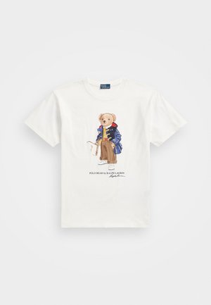 Hvid T-shirt med en bamse iført en marineblå jakke, brune bukser, hvide sko, der holder en golfkølle, med teksten "Polo Bear by Ralph Lauren".