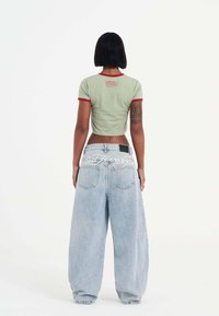 Lichtgroene crop top met rode bies; de achterkant heeft een kleine grafische print. Hoog in de taille, losse lichtblauwe denim jeans met grote zakken.