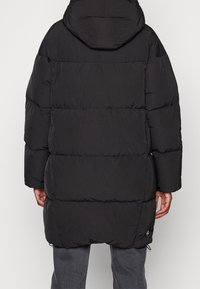 Black puffer jacket with a hood, featuring a quilted design and loose fit. Includes side zippers and elastic cuffs for warmth.