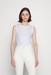 Top branco sem mangas com um decote redondo, combinado com jeans brancos de cintura alta. Tecido suave com uma silhueta ajustada. Design simples e minimalista.