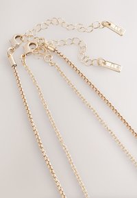 Gold-tone metal chain with varying link styles. Features clasp closures and decorative accents, including small rectangular charms with stones.