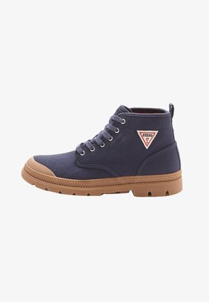Baskets montantes bleu marine avec semelle en caoutchouc marron, embout, œillets métalliques, lacets et un logo triangulaire Guess sur le côté.