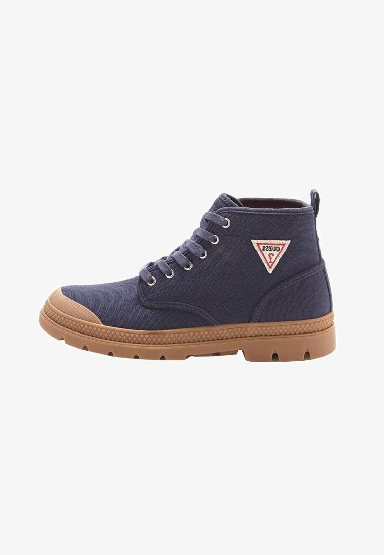 Baskets montantes bleu marine avec semelle en caoutchouc marron, embout, œillets métalliques, lacets et un logo triangulaire Guess sur le côté.