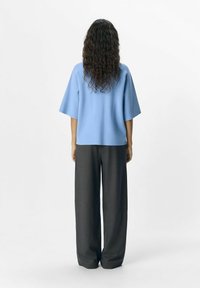 Haut bleu clair à manches courtes avec une coupe décontractée, assorti à un pantalon large gris foncé. Le tissu a l'air lisse avec une texture douce.