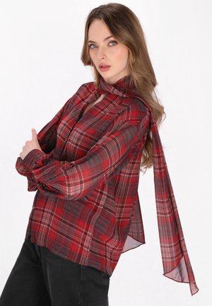 Blusa leggera rossa e a quadri con collo alto e maniche lunghe. Presenta un tessuto trasparente e un fiocco al collo.