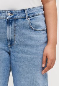 Gai zila džinsu bikses ar augstu jostasvadu, klasisku piecu kabatu dizainu, smalku dūrienu un sudraba pogu aizdari. Gluda tekstūra.