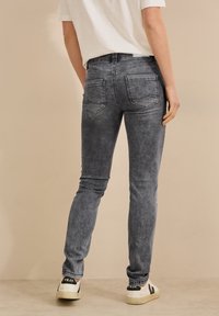 Hoikat harmaan denim-farkut, joissa on haalistunut pinta, kahdella takataskulla ja keskikorkealla vyötäröllä. Yhdistetty valkoisiin lenkkareihin.