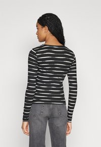 Long-sleeve top with a black and white striped pattern, rounded neckline, and fitted design. Soft, stretchy fabric. Back view displayed.