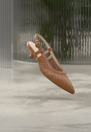 Bruine geweven leren slingback schoen met lage hak en gesp, zwevend boven een betonnen vloer met een wazige achtergrond met verticale strepen.