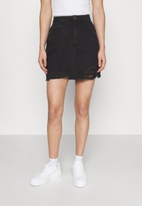 Gonna di jeans nera con vita alta, tasche frontali, strappi consumati e orlo grezzo, abbinata a sneakers bianche con plateau.