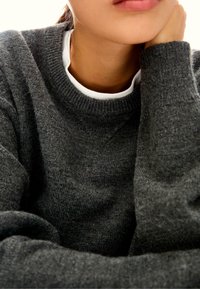 Maglione grigio lavorato a maglia con collezione rotonda indossato sopra una camicia bianca, che mostra una texture morbida e dettagli sottili nella trama del tessuto.