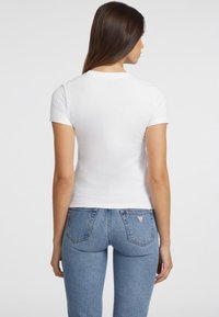 Witte T-shirt met korte mouwen en een ronde hals, gecombineerd met slim-fit blauwe denim jeans met een driehoekig logo op de achterkant.