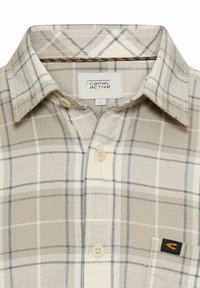 Beige karierte Hemd mit Button-Down-Kragen. Mit hellblauen und grauen Linien, zwei vorderen Knöpfen und einem kleinen schwarzen Logo auf der Tasche.