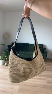 Beige woven bag with a textured finish, featuring a black leather strap and an open top design. Minimalist and functional style.