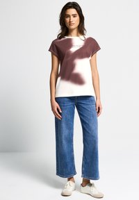 Hvid og burgundy tie-dye kortærmet t-shirt med løstsiddende pasform, parret med højtaljede blå brede jeans og hvide sneakers.
