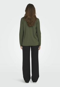 Oliwkowy top z długimi rękawami, o prostym kroju. Połączony z czarnymi szerokimi spodniami i białymi trampkami.