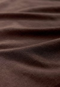 Brūns audums ar gludu tekstūru, kurā ir smalkas krokas un locījumi, liecinot par mīkstu un lokanu materiālu.